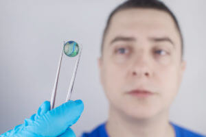 An eye surgeon holds a multifocal lens for cataract treatment near the patient.