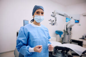 Female cataract surgeon in operating room at ophthalmology clinic looking at camera.