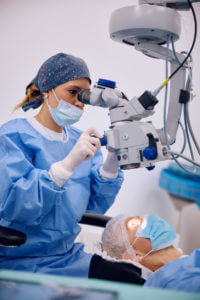 Medical eye expert looking through microscope during cataract eye surgery at ophthalmology clinic.